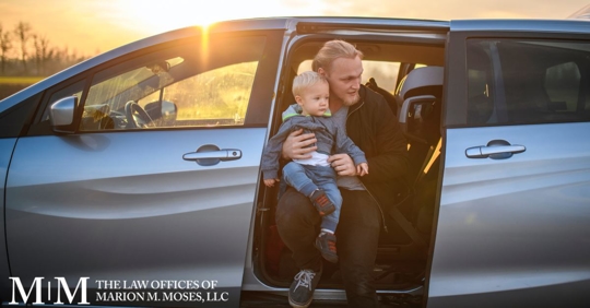 Man sitting on back seat in minivan with child on his lap, looking out the open door