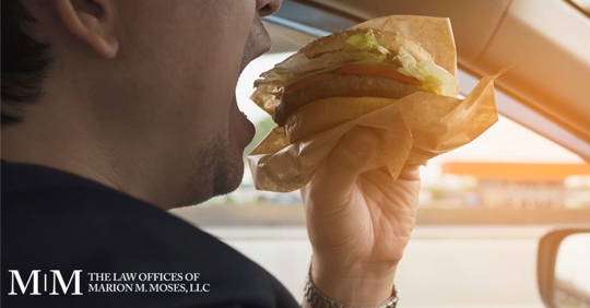 man driving and taking a bite of a burger